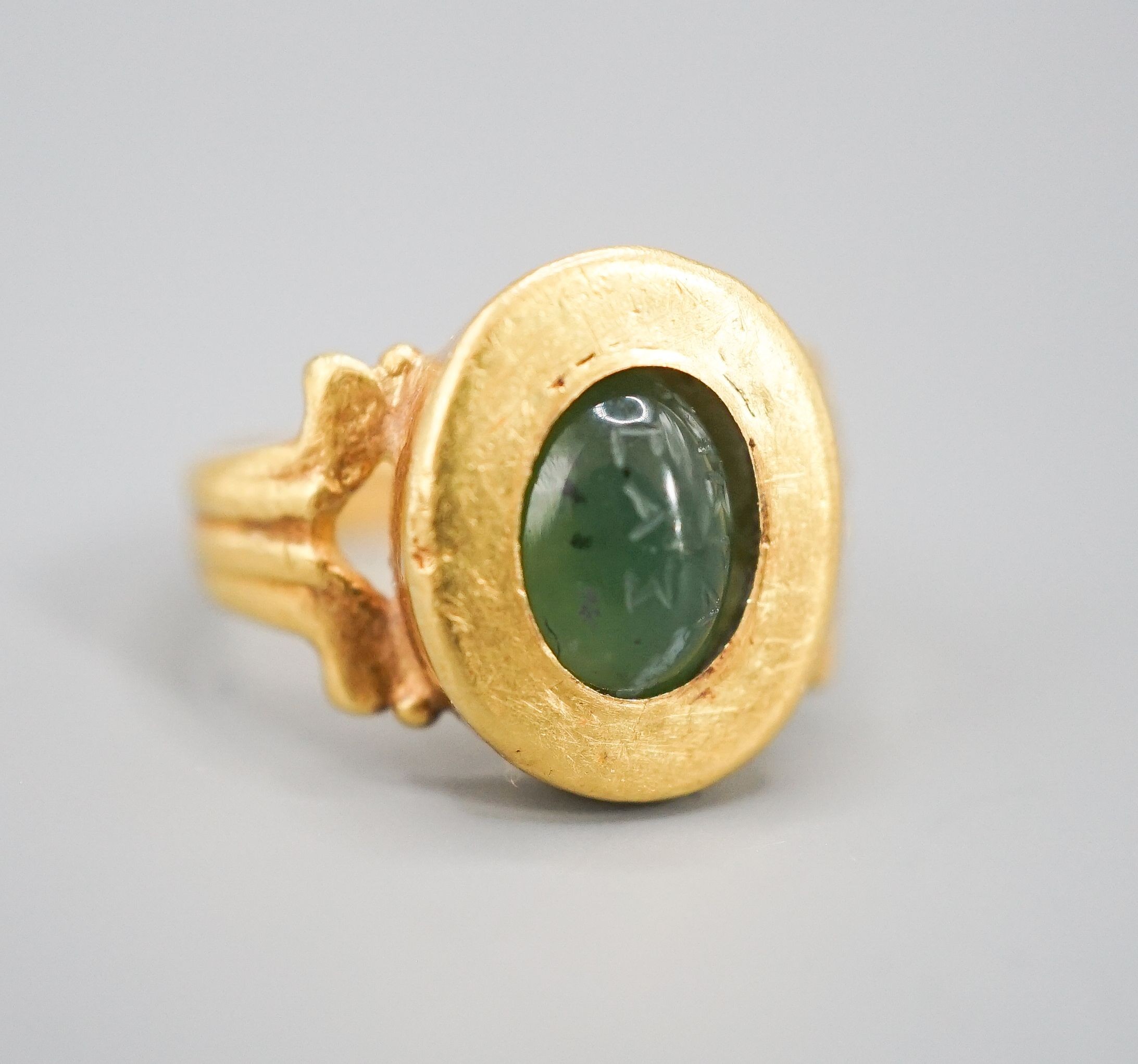 An antique yellow metal and carved nephrite? oval ring, size H, gross 4 grams (the stone is loose in situ and needs re-setting).